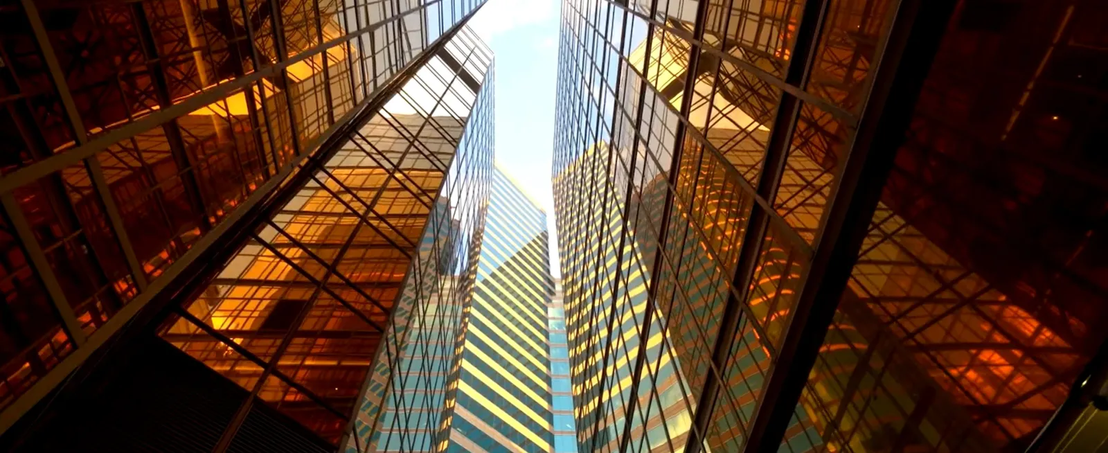 Looking up between two reflective glass buildings with golden hues, showing a clear sky above.