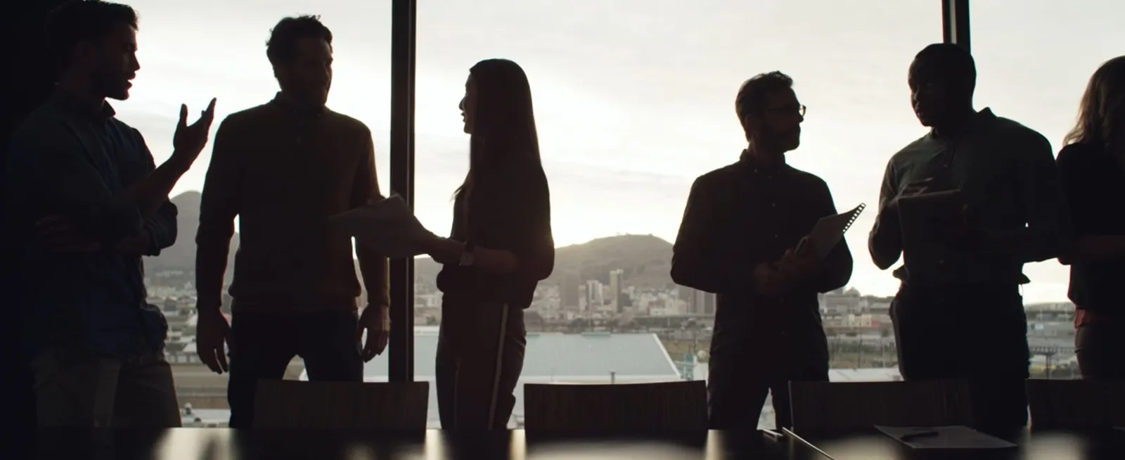 Silhouetted group of people talking near a window with a cityscape in the background.