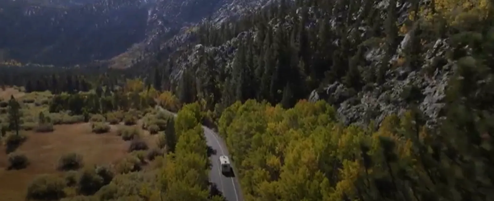 Car on a winding road surrounded by trees and rocky mountains in an autumn landscape.