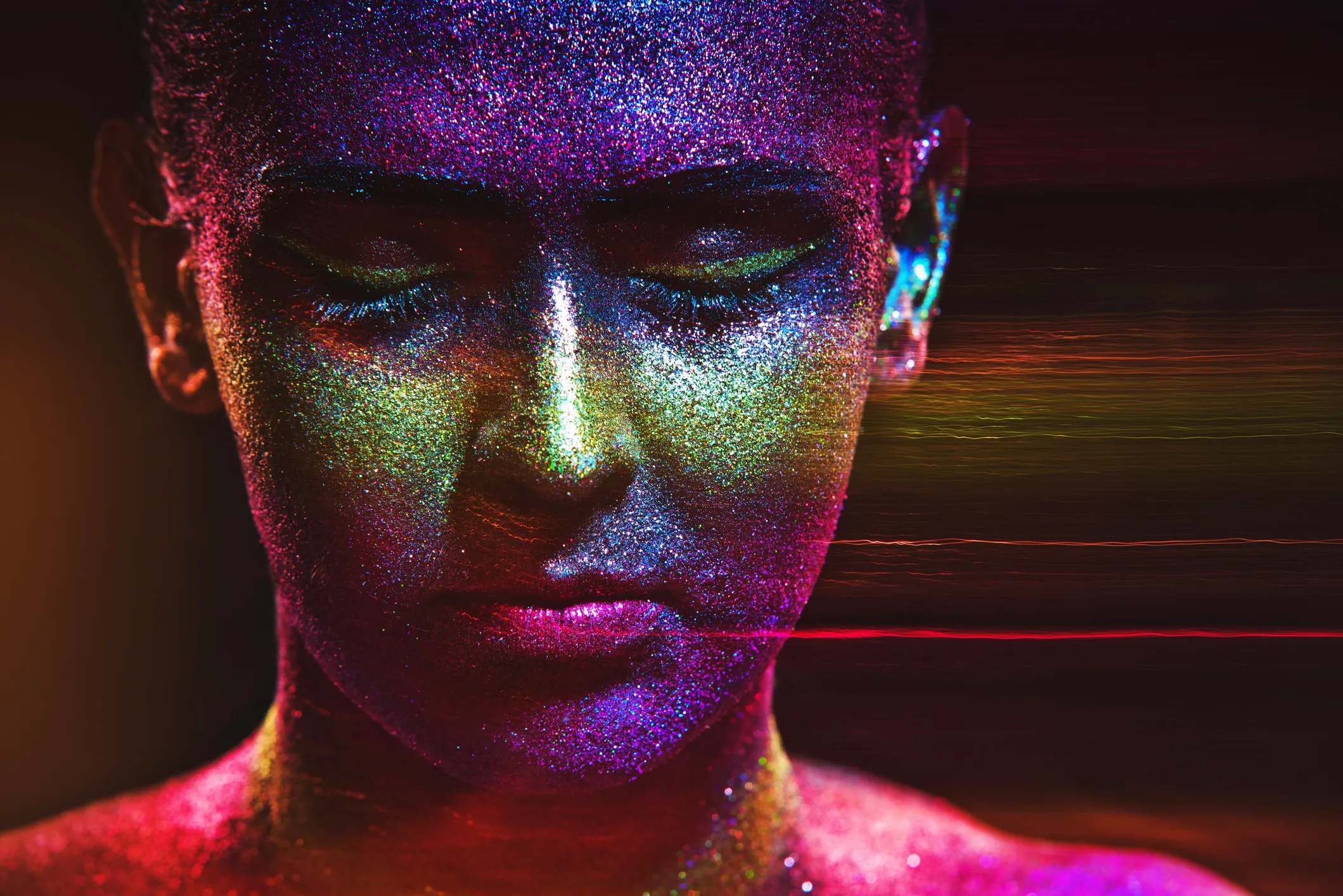 Face covered in multicolored glitter, eyes closed, illuminated by dynamic streaks of vibrant light.